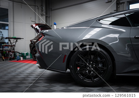 Rear view of a gray Ford Mustang GT 5.0 with black alloy wheels, parked on a checkered floor in a well lit garage with tools and equipment visible. Rear view of a gray Ford Mustang GT 5.0 with black alloy wheels, parked on a checkered floor in a well lit garage with tools and equipment visible. 129561015
