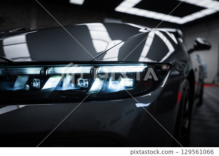 Front headlight of a Ford Mustang GT 5.0 with illuminated LED design, glossy metallic finish, and reflections from showroom ceiling lights. Front headlight of a Ford Mustang GT 5.0 with illuminated LED design, glossy metallic finish, and reflections from showroom ceiling lights. 129561066
