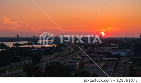 Warm sunset over Riga, Latvia, featuring the Riga TV Tower, old town spires, Daugava River, a bridge, urban roads, buildings, and greenery. 129561078