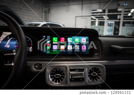 Mercedes AMG G Class interior showing Apple CarPlay on the infotainment screen, metallic air vents, leather dashboard with red stitching, and a garage setting. 129561131