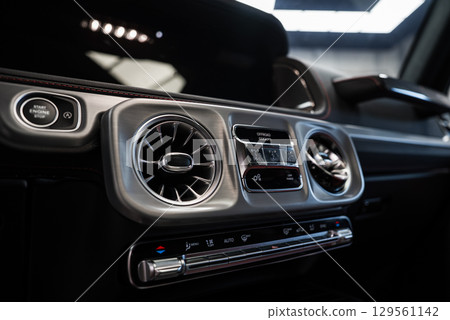 Close up of Mercedes AMG G Class interior showing circular air vents, digital display, Start Engine Stop button, and red stitched leather trim. Close up of Mercedes AMG G Class interior showing circular air vents, digital display, Start Engine Stop button, and red stitched leather trim. 129561142