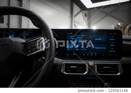 Close up of a vehicle's dashboard featuring a digital display with a navigation map in Russian, metallic air vents, and a sleek steering wheel design. 129561146