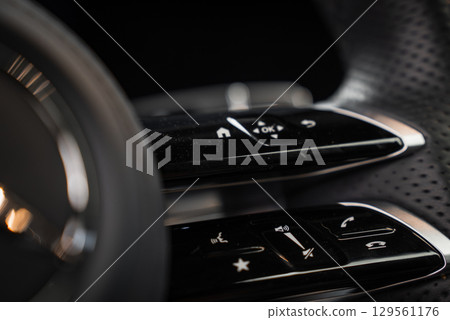Detailed view of steering wheel controls in a Mercedes AMG G Class, featuring glossy black finish, chrome accents, and perforated leather texture. Detailed view of steering wheel controls in a Mercedes AMG G Class, featuring glossy black finish, chrome accents, and perforated leather texture. 129561176