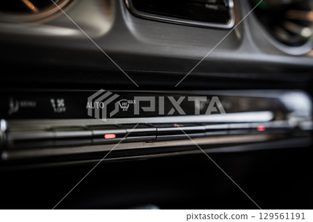Detailed view of the climate control panel in a Mercedes AMG G Class, featuring metallic buttons, illuminated indicators, and air vents in the background. 129561191