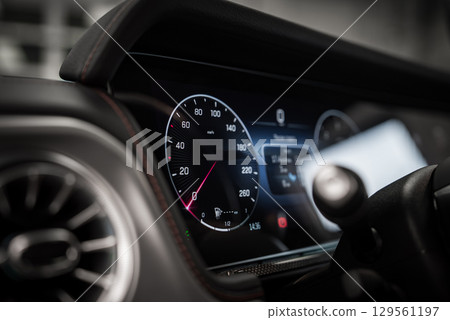 Close up view of a car dashboard featuring a digital speedometer, red stitched trim, metallic air vent, and high resolution displays indoors. 129561197