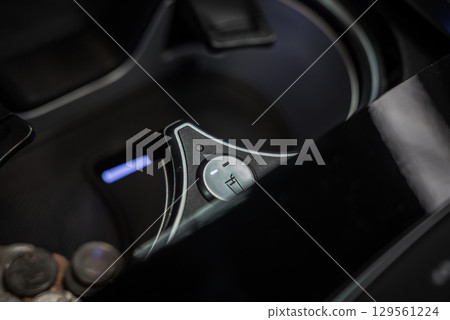Close up view of a metallic cup holder cooling control dial near a cup holder in a car interior. Glossy black finish surrounds the area, with coins visible nearby. Close up view of a metallic cup holder cooling control dial near a cup holder in a car interior. Glossy black finish surrounds the area, with coins visible nearby. 129561224
