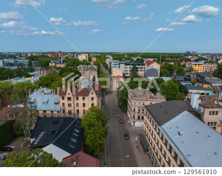 Aerial view of a Riga street lined with historic buildings in Jugendstil style, flanked by green trees, with a skyline of modern and older structures. Aerial view of a Riga street lined with historic buildings in Jugendstil style, flanked by green trees, with a skyline of modern and older structures. 129561910
