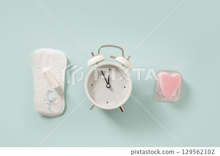 Female different tampons, daily pads, clock on blue background. Limited time use concept. Hygiene accessories for women. View from above. 129562102