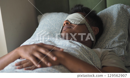 Person resting in bed with sleep mask on 129562907