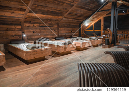 Cozy room with wooden walls, daybeds, curved lounge chairs, and large windows. Soft lighting and natural materials create a serene alpine ambiance. Cozy room with wooden walls, daybeds, curved lounge chairs, and large windows. Soft lighting and natural materials create a serene alpine ambiance. 129564339