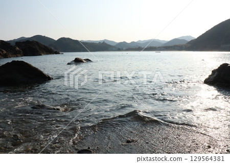 Calm sea and rock silhouettes - Coastal scenery bathed in the morning glow 129564381