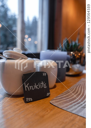 Cozy indoor scene with a wooden table, ceramic teapot, sugar bowl, succulent plant, and snowy outdoor view through a large window in warm lighting. Cozy indoor scene with a wooden table, ceramic teapot, sugar bowl, succulent plant, and snowy outdoor view through a large window in warm lighting. 129564389
