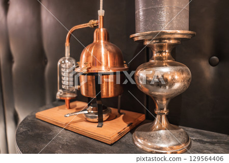 A small copper distillation apparatus on a wooden base, paired with a metallic decorative piece. Dark tufted leather background adds a luxurious touch. A small copper distillation apparatus on a wooden base, paired with a metallic decorative piece. Dark tufted leather background adds a luxurious touch. 129564406