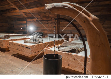 Cozy spa area in the Italian Alps with wooden walls, daybeds, and a sculptural water feature dripping into a black metal basin under soft lighting. Cozy spa area in the Italian Alps with wooden walls, daybeds, and a sculptural water feature dripping into a black metal basin under soft lighting. 129564421