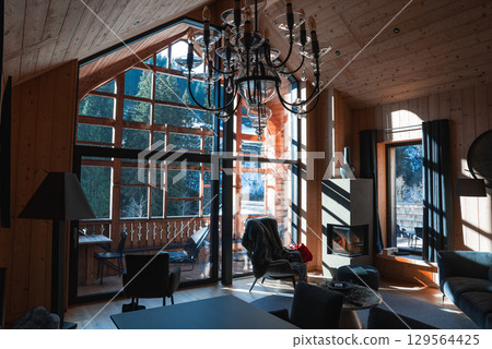 Interior of a luxury hotel suite in the Italian Alps with a sloped wooden ceiling, large windows, a chandelier, modern furnishings, and snowy views. 129564425