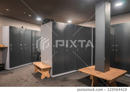 A sleek locker room featuring dark gray lockers, wooden benches, a central wooden table, and soft lighting, located in a luxury hotel in the Italian Alps. A sleek locker room featuring dark gray lockers, wooden benches, a central wooden table, and soft lighting, located in a luxury hotel in the Italian Alps. 129564428
