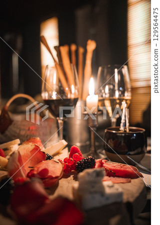 A rustic wooden table features a charcuterie board, wine glasses, breadsticks, and a lit candle, set in a cozy, dimly lit Alpine hotel setting. 129564475