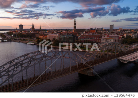 Riga, Latvia at sunset with the Daugava River, Railway Bridge, and Old Town landmarks like St. Peter's Church and Riga Cathedral in the background. Riga, Latvia at sunset with the Daugava River, Railway Bridge, and Old Town landmarks like St. Peter's Church and Riga Cathedral in the background. 129564476