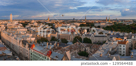 Riga, Latvia, at sunset featuring the historic old town, Jugendstil architecture, Riga TV Tower, church spires, green spaces, and a bird in flight. 129564488