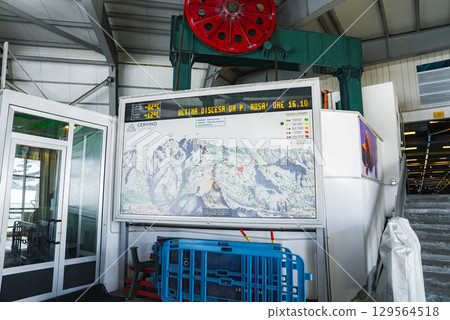 Modern ski lift station featuring a detailed ski area map, a red pulley wheel, digital displays, and a blue barrier in Zermatt Cervinia. 129564518