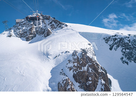 A ski lift station atop a rugged peak in Zermatt, Switzerland, surrounded by steep snow covered slopes, jagged rocks, and clear blue skies. A ski lift station atop a rugged peak in Zermatt, Switzerland, surrounded by steep snow covered slopes, jagged rocks, and clear blue skies. 129564547