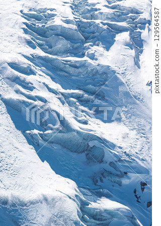 Aerial view of a glacier in Zermatt, Switzerland, featuring icy crevices, undulating formations, and a mix of deep blue and white hues. 129564587