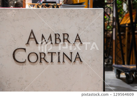 Marble desk with raised lettering 'AMBRA CORTINA', books, pinecone, and warm lighting in a boutique hotel in Cortina, Dolomites, Italy. 129564609
