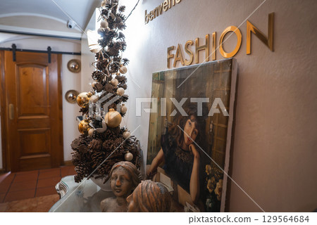 A boutique hotel corner in Cortina, Dolomites, Italy, featuring a small Christmas tree, gold ornaments, framed portrait, and welcoming Italian decor. 129564684