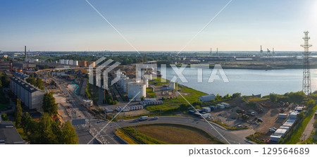 View of an industrial zone near a river in Riga, Latvia, featuring storage tanks, cranes, a shipyard, a curved road, and a tall transmission tower. View of an industrial zone near a river in Riga, Latvia, featuring storage tanks, cranes, a shipyard, a curved road, and a tall transmission tower. 129564689