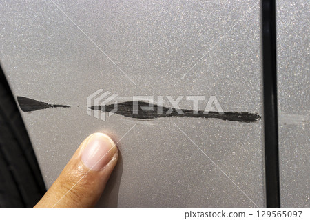A man's hand pointing to a scar on the car body 129565097