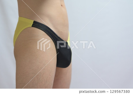 Man in yellow and black swimsuit standing sideways 129567380