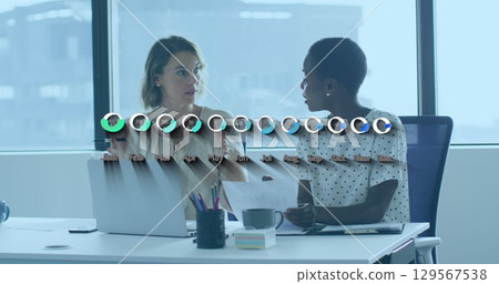 Image of financial data and graphs over diverse female coworkers working in office 129567538