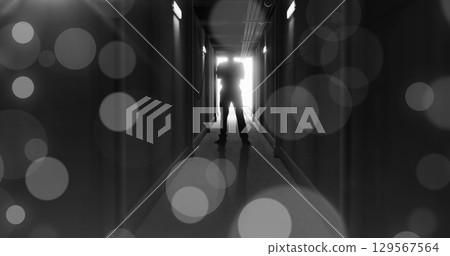 Image of grey bokeh light spots over scary figure backlit in doorway at end of dark corridor Image of grey bokeh light spots over scary figure backlit in doorway at end of dark corridor 129567564