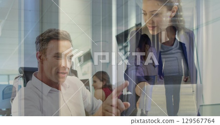Image of coworkers discussing over laptop in office and colleagues walking in corridor Image of coworkers discussing over laptop in office and colleagues walking in corridor 129567764