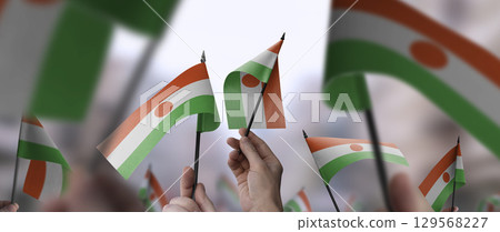 Niger flags in their hands on a blurred urban background 129568227