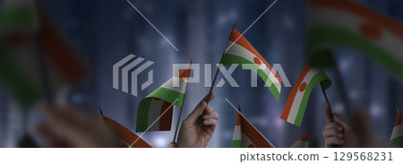 Niger flags in their hands on a blurred urban background Niger flags in their hands on a blurred urban background 129568231