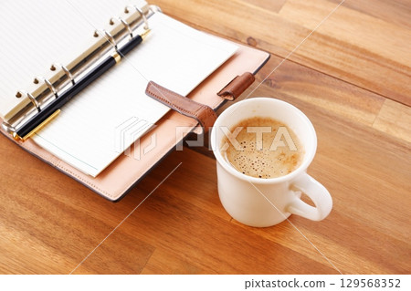 Image of a man working at his desk with a system organizer while drinking a cafe latte, a coffee with plenty of milk Image of a man working at his desk with a system organizer while drinking a cafe latte, a coffee with plenty of milk 129568352