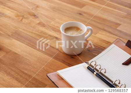 一張圖片：某人在辦公桌前使用筆記本工作，同時喝著加大量牛奶的咖啡或拿鐵咖啡。 129568357