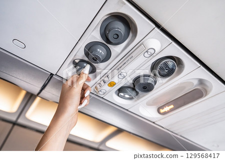 Passenger Adjusting Air Vent on Airplane Ceiling for Comfortable Flight Experience 129568417