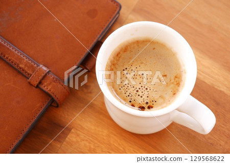 An image of someone writing in a diary while drinking a cafe latte, a coffee with plenty of milk. 129568622