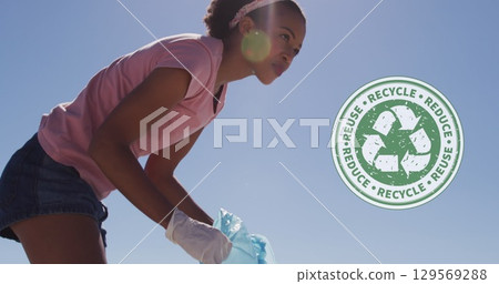 Image of recycling symbol over african american woman cleaning at beach 129569288