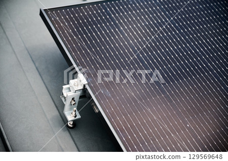 Close up of solar panel, securely fastened with robust mounting clamp to supporting structure on rooftop of house. Bolts and clamps provide stability and durability to solar installation. Close up of solar panel, securely fastened with robust mounting clamp to supporting structure on rooftop of house. Bolts and clamps provide stability and durability to solar installation. 129569648