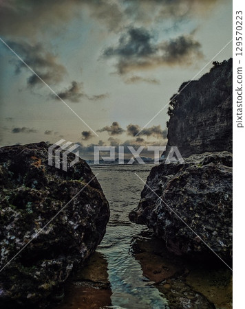 A moody and atmospheric photo of a rocky coastline at sunset. The dark clouds and choppy water create a sense of dramatic nature. 129570223