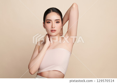 Beautiful Young Asian woman Raises her hands to Showcase clean and hygienic underarms Against a beige background, Smooth armpit cleanliness and protection concept 129570514
