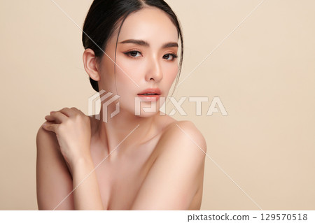 A beautiful young Asian woman with clean, fresh skin against a beige background. Skincare, facial treatment, cosmetology, beauty, and spa. An elegant portrait of an Asian woman. 129570518
