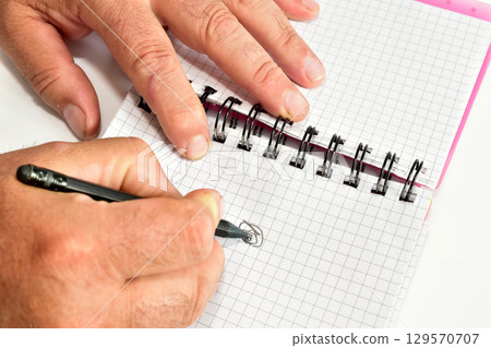 A man's hand writes in a notebook. 129570707