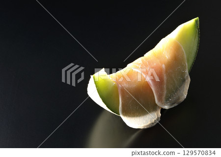Raw ham and melon photographed against a black background 129570834