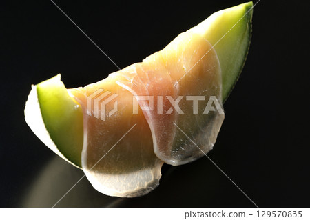 Raw ham and melon photographed against a black background 129570835