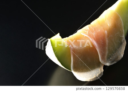 Raw ham and melon photographed against a black background 129570838