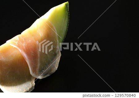 Raw ham and melon photographed against a black background 129570840